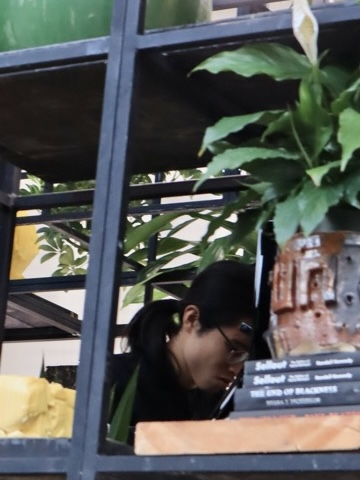 Alexander playing the piano behind plants, shea butter, and a few books titled “Sellout” placed on black shelves