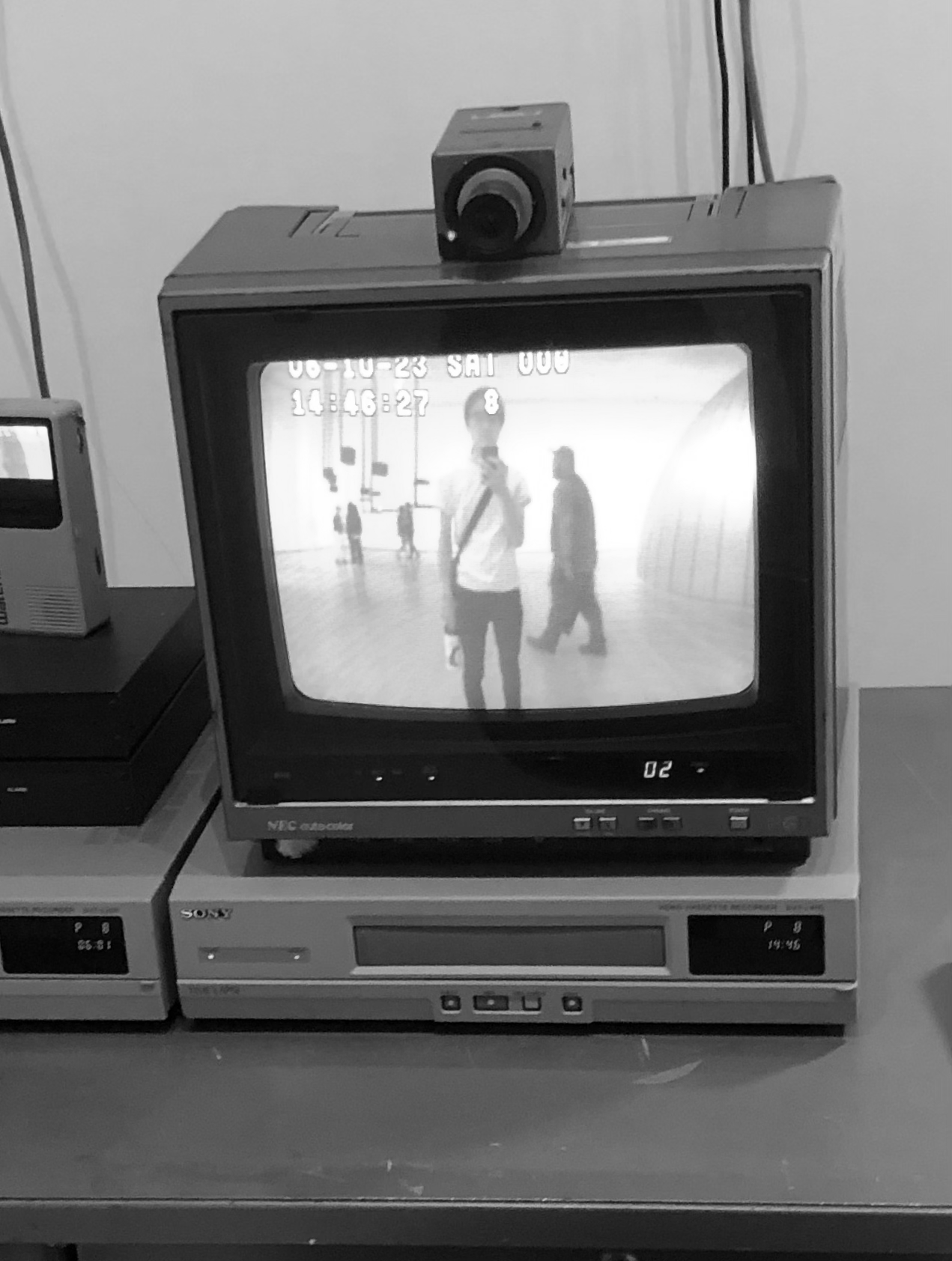 A CCTV monitor with a camera above it showing an image of Alexander holding his phone standing in front